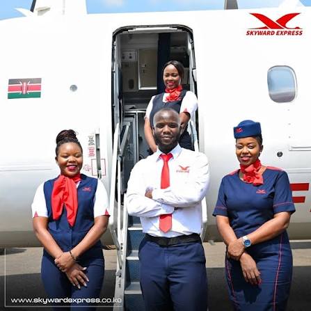Skyward Airlines crew in navy and red uniforms at the open doorway of a Skyward aircraft flying the Kenyan flag